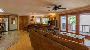 Ein geräumiges Wohnzimmer mit einem großen braunen Sofa, einem Essbereich mit Holzkästen, einer Küche mit Holzsäulen und einem Balkon mit Geländer.