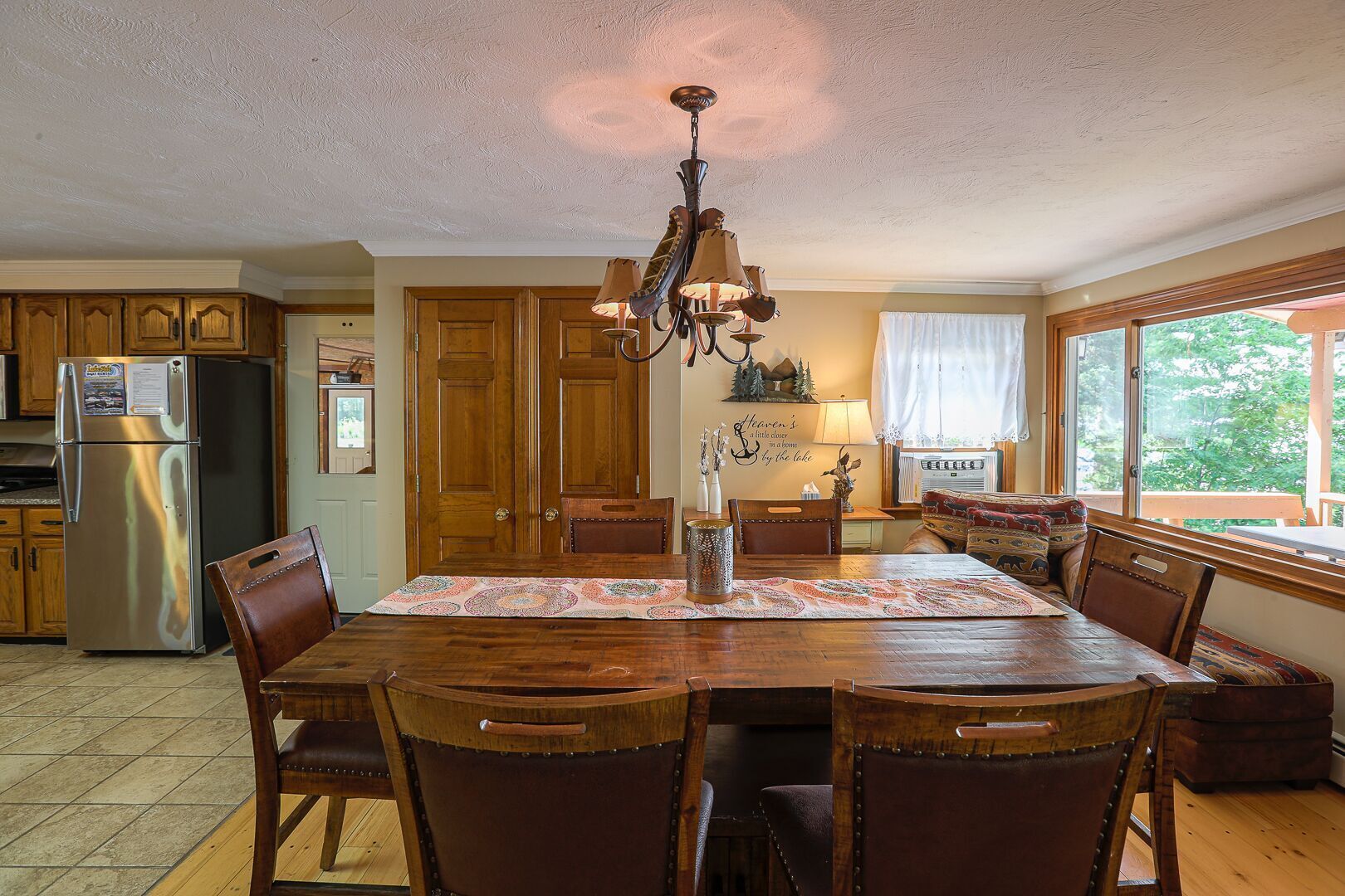 A spacious kitchen with wooden cabinets, a stainless steel refrigerator, a chandelier, and a dining table set for six.