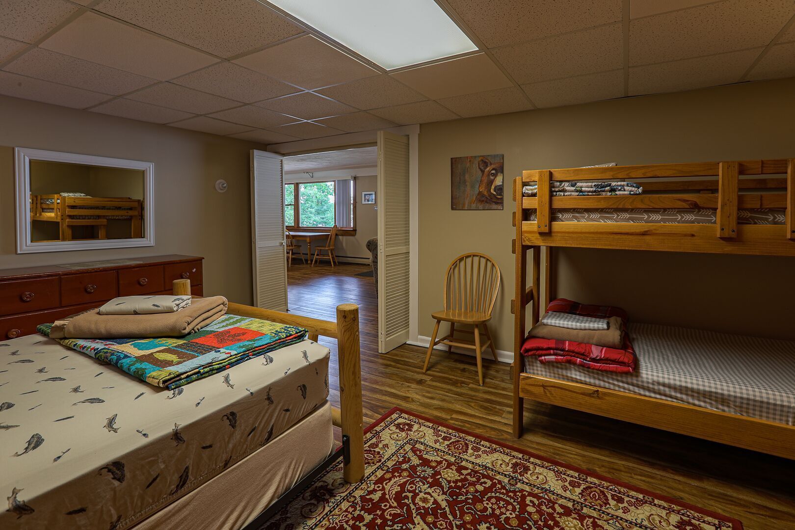 A bedroom with a bunk bed, a single bed, a wooden dresser, a chair, and a painting on the wall.