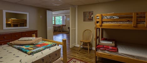A bedroom with a bunk bed, a single bed, a wooden dresser, a chair, and a painting on the wall.