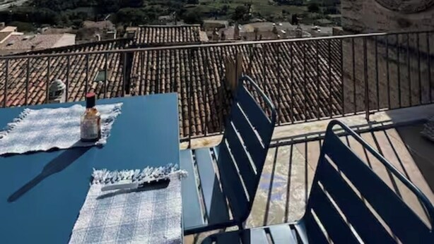 Een terras met uitzicht op het landschap, een klok aan de muur en een tafel met een fles en glazen.