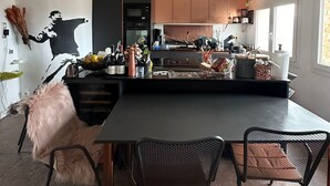 Een moderne keuken met een centraal eiland, hanglampen en een eethoek met stoelen.
