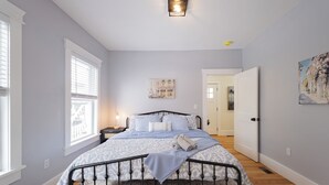 Quarto com cama, mesa de cabeceira, janela e porta.