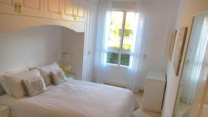A bedroom with a large bed, a nightstand, a dresser, and a window with curtains. - 2 bed Apt, grt Location, Shared Pool, Outdoor Area (Javea)