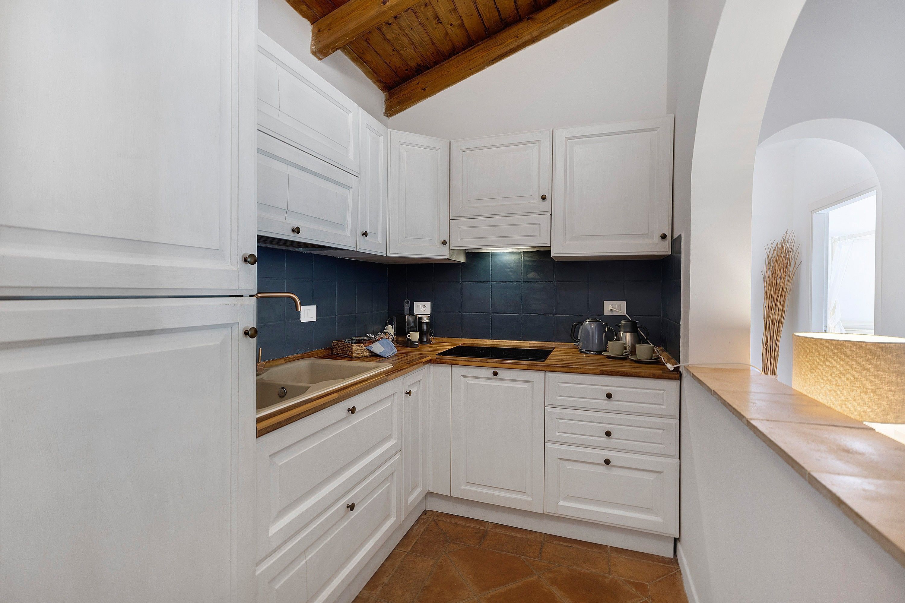 Una cocina con armarios blancos, encimera de madera y salpicadero de azulejos.