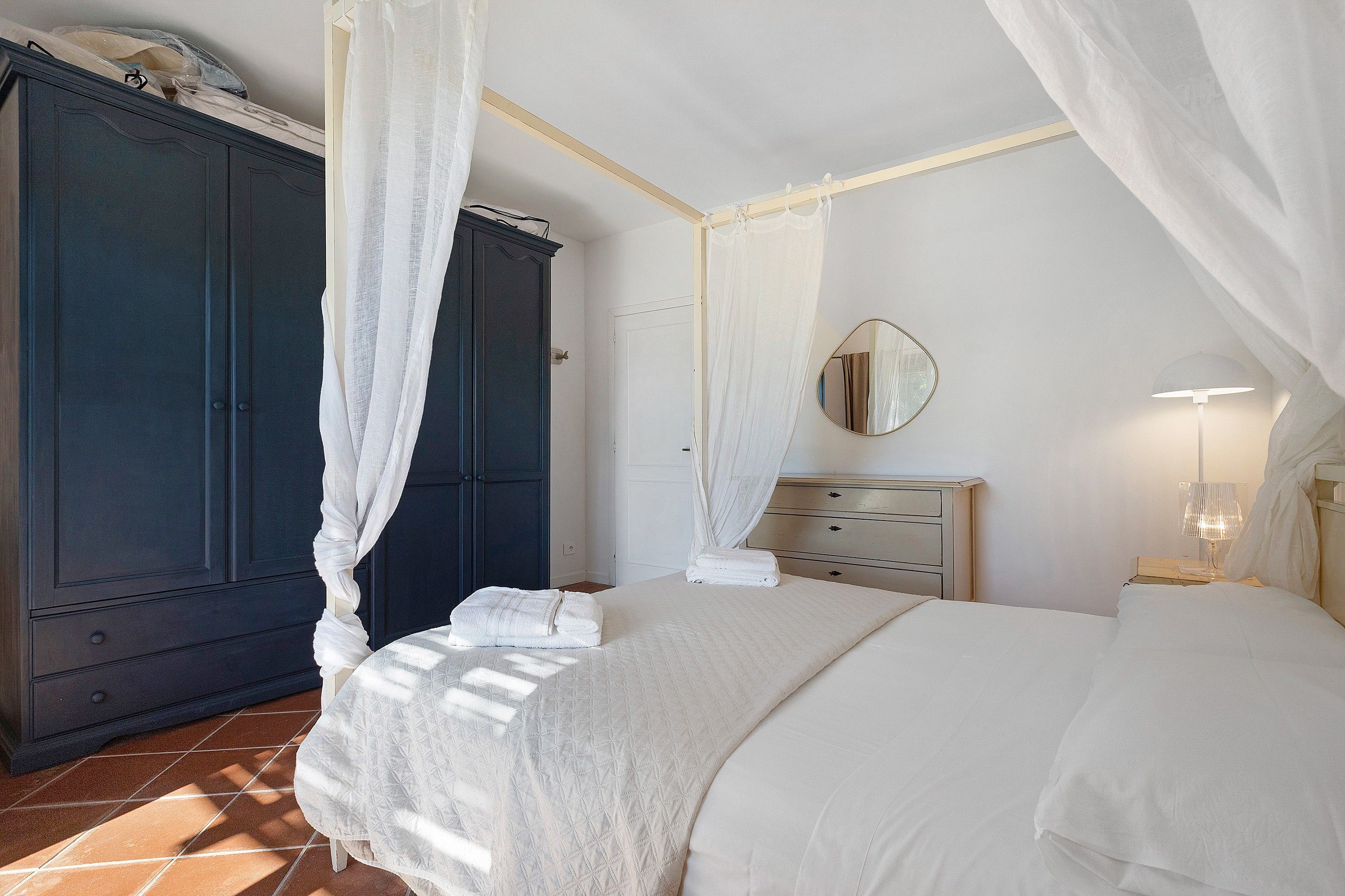 Un dormitorio con cama, armario, espejo y mesita de noche con lámpara.
