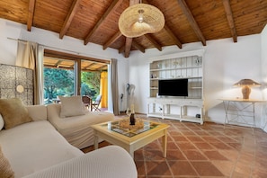 A living room with a sofa, a television, and a table with a bottle. - Villa 'Sole Con Piscina Privata' with Private Pool, Wi-Fi and Air Conditioning (Punta de Su Turrione)