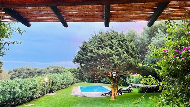 Un espacio al aire libre techado con piscina, sillas de descanso y un pérgola.