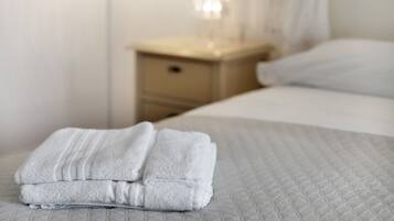 A neatly made bed with a folded white towel on top, a bedside table with a lamp, and a white wall.