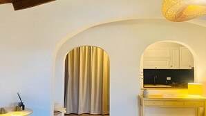 Una habitación con techo de madera, una zona de cocina con una lámpara amarilla, una mesa de comedor con sillas y suelo de baldosas.