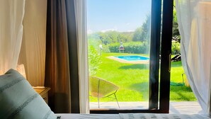 Un dormitorio con cama, una silla y vistas a una piscina y vegetación.