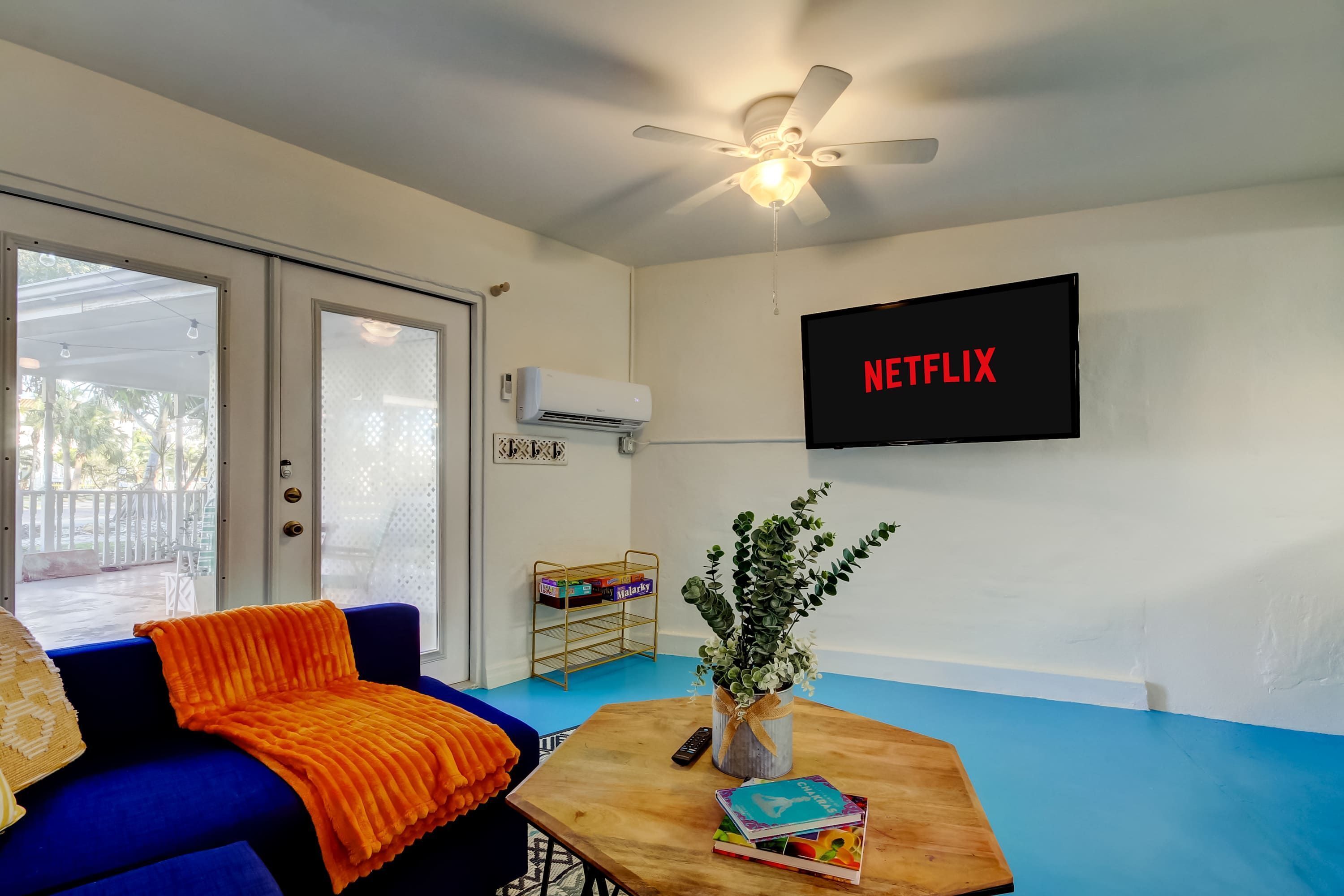 A living room with a blue couch, a wooden coffee table, a plant, and a TV displaying the Netflix logo.