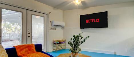 A living room with a blue couch, a wooden coffee table, a plant, and a TV displaying the Netflix logo.
