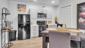 A modern kitchen with white cabinets, a black refrigerator, and a microwave. There is a dining table with chairs and a vase with flowers.