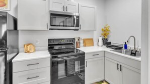 A modern kitchen with white cabinets, a stainless steel refrigerator, a microwave, an oven, and a sink.