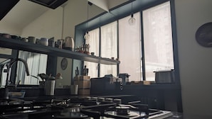 A kitchen with a gas stove, a sink, and a window with curtains. There are shelves with kitchen utensils and a clock on the wall. - Stica Loft Apartment (Milano)