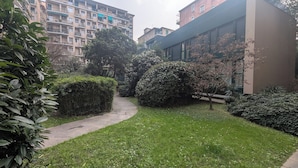 A courtyard with a paved path, neatly trimmed hedges, and a building with large windows. - Stica Loft Apartment (Milano)