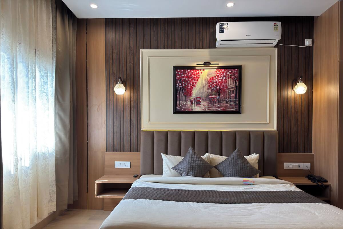 A hotel room with a bed, bedside tables, an air conditioner, and a painting on the wall.
