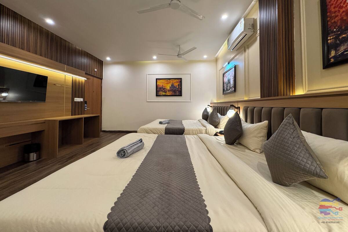 A hotel room with two beds, a TV, a ceiling fan, and artwork on the walls.