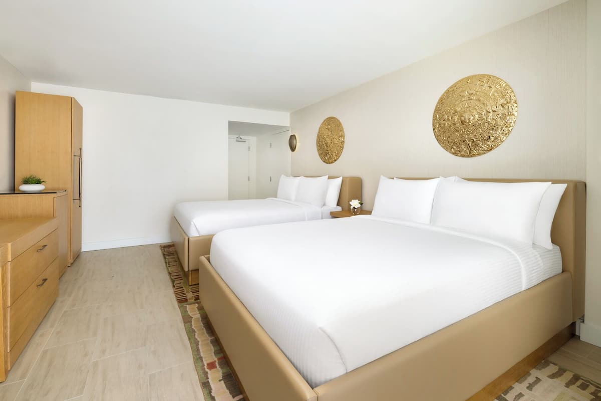 Habitación de hotel con dos camas, un aparador de madera, un espejo y decoración en las paredes.