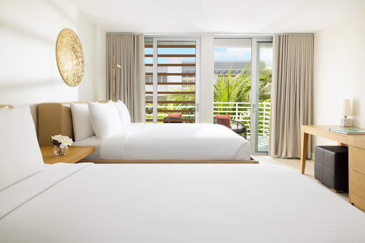 Habitación de hotel con cama, escritorio, silla, una pequeña mesa con un florero y vistas al exterior.