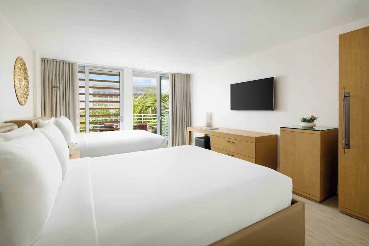 Habitación de hotel con una cama grande, un escritorio, un armario, un televisor y un balcón con cortinas.