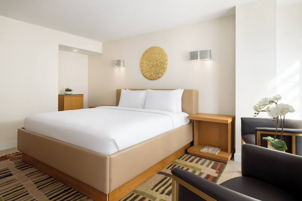 Una habitación de hotel moderna con una cama grande, una mesita de noche de madera, una pequeña mesa con un florero y una silla.