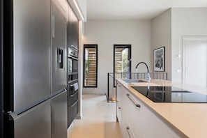 A modern kitchen with a stainless steel refrigerator, a black countertop, and a window with blinds.