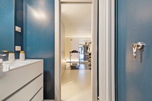 Une salle de bain avec un mur bleu, un lavabo blanc et une porte donnant sur un couloir.