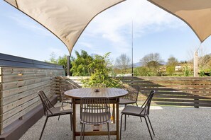 Une terrasse extérieure avec une table ronde et des chaises, entourée d’une clôture en bois et d’un grand auvent.