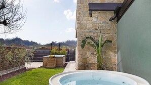 Ein Whirlpool in einem Garten mit einer Steinmauer, einer Holzterrasse und Blick auf eine hügelige Landschaft.