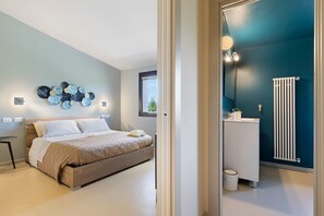 Une chambre à coucher moderne avec un lit, une table de chevet, des œuvres d’art murales et une vue sur la salle de bain.