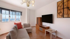 Un salon moderne avec un canapé, un téléviseur, un meuble en bois et une grande fenêtre.