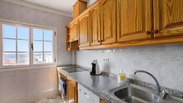A kitchen with wooden cabinets, a granite countertop, a built-in dishwasher, and a window with a city view.