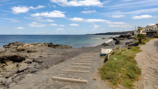 Un sentier côtier avec des marches menant à une plage rocheuse, un ciel dégagé et des éoliennes visibles au loin.