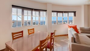Un espace repas comprenant une table et des chaises, un canapé et de grandes fenêtres offrant une vue dégagée.