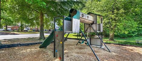 A playground with a climbing structure, a slide, and a swing set.