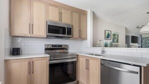 Una cocina moderna con armarios de madera clara, electrodomésticos de acero inoxidable y un salpicadero de azulejos blancos.
