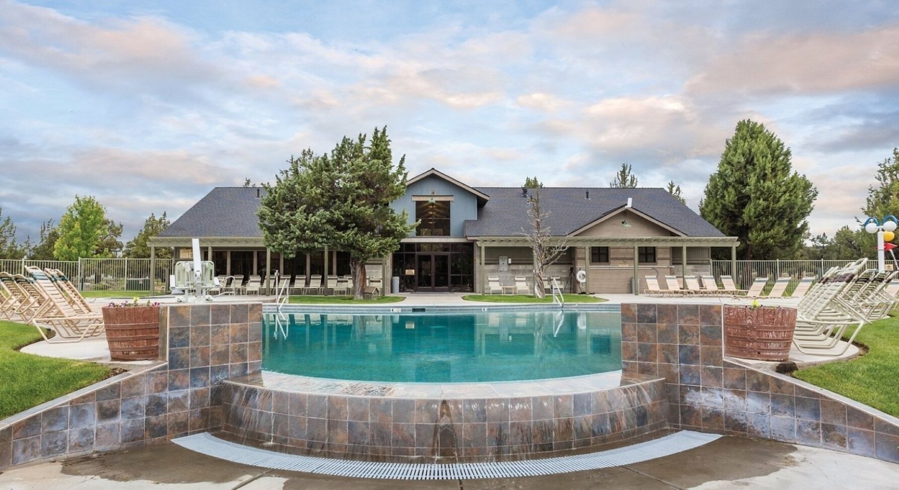 Une piscine bordée de pierres, un patio couvert et, au fond, un bâtiment doté d’un toit en pente.