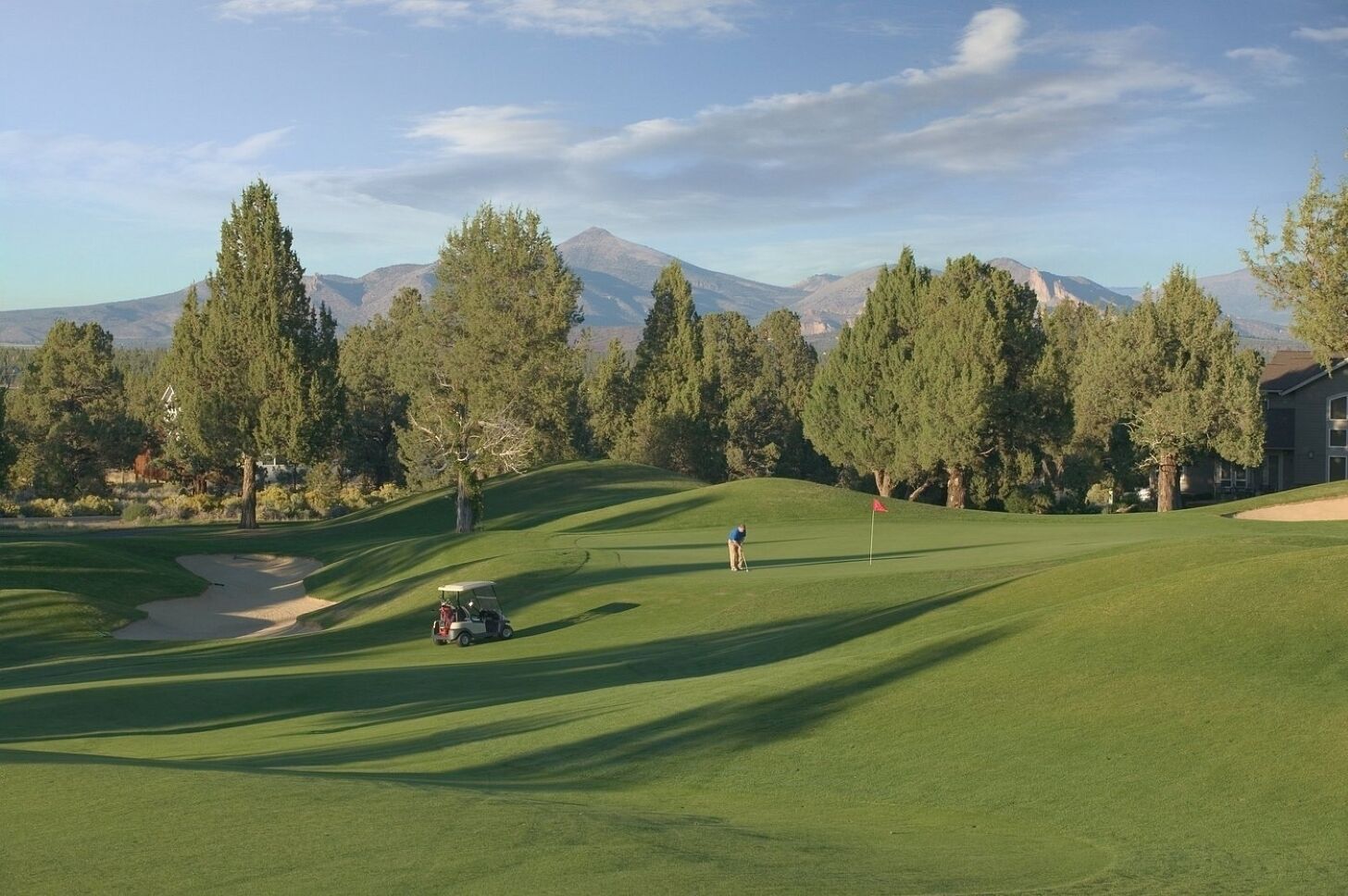 A golf course with a clubhouse, trees, and mountains in the background.