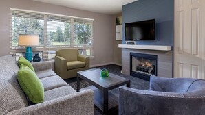 Een woonkamer met een open haard, een televisie erboven en een bank met een groen kussen.