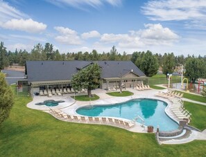 A large swimming pool with a deck area, surrounded by a covered patio and a grassy lawn. - Redmond | High Desert Scenic Stay | Pool + Trails | 2BR Upper Floor (Redmond)