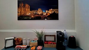 A framed cityscape painting, a coffee maker, a water bottle, and a tea box on a table. - A due Passi Dal Centro (Noto)