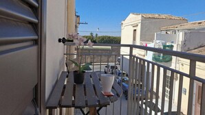 A balcony with a wooden table, potted plants, and a view of parked cars and buildings. - A due Passi Dal Centro (Noto)