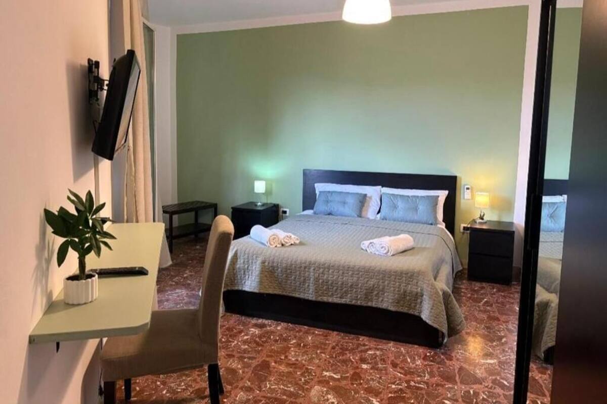 A hotel room with a bed, a desk, a chair, a potted plant, and a nightstand.