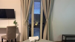 A hotel room with a bed, a chair, a TV, a window with curtains, and a small table. - A due Passi Dal Centro (Noto)