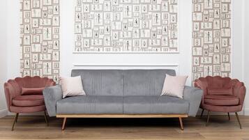 A modern living room with a grey sofa, two pink armchairs, and a wall decorated with framed sketches.