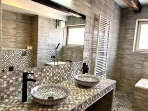 Casa de banho com duas pias redondas, um espelho grande e um painel de azulejos.