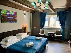 Ett hotellrum med en säng, två stolar, ett bord, en tavla och ett fönster med gardiner.