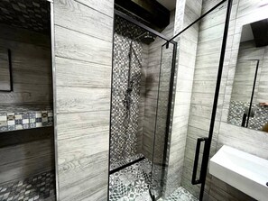 Ein modernes Badezimmer mit Dusche, Fliesen und einem weißen Waschbecken.